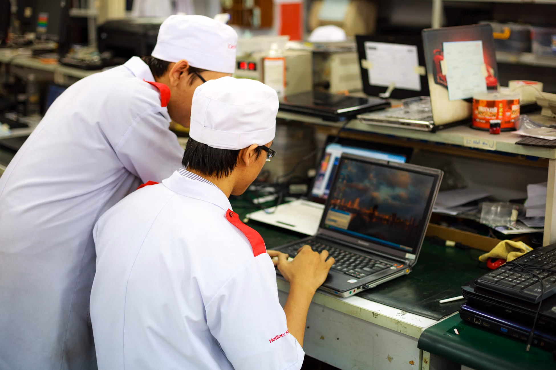 Two technicians in uniforms working on laptops in a laboratory setting. Focus on teamwork and technology.