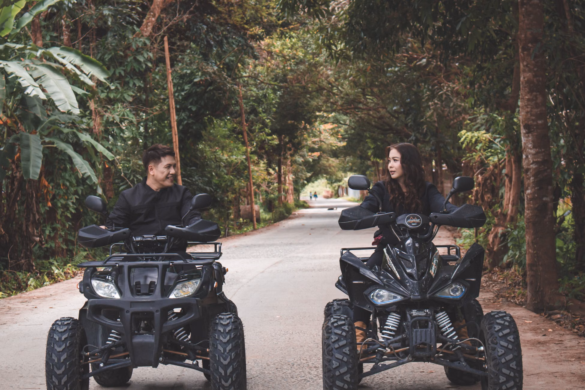 A couple enjoying a scenic ride on quad bikes through a lush green path.