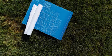 Top view of architectural blueprints on a grassy field, ideal for construction themes.