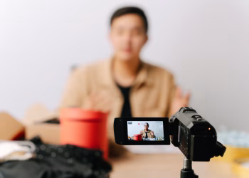 A blogger sits in front of a camera for filming a video indoors.