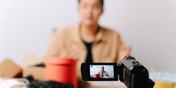 A blogger sits in front of a camera for filming a video indoors.