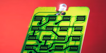 Close-up of a green circuit with intricate patterns on a vibrant red background, ideal for technology themes.