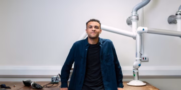 Confident young engineer standing in a laboratory with advanced robotic equipment.