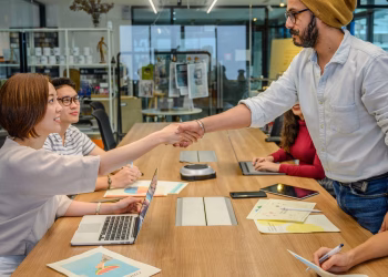 Diverse professionals in a modern office engaged in a collaborative meeting, shaking hands across a conference table.