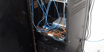 EFTA00002004 - Open server rack with blue and orange cables connected to networking equipment in a utility room
