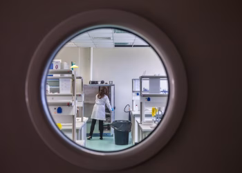 A female scientist in a lab coat working inside a state-of-the-art laboratory through a circular window view.