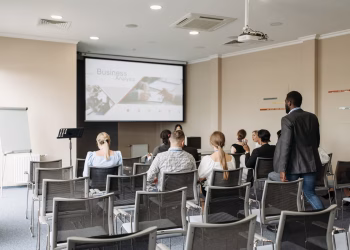 Business conference attendees listening to a presentation in an office setting.