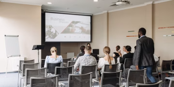 Business conference attendees listening to a presentation in an office setting.
