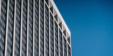 Low angle facade of contemporary multistory skyscraper with many windows against blue sky