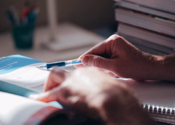 Close-up of hands writing in a notebook with a pen on a desk, suggesting focus and learning.