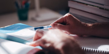 Close-up of hands writing in a notebook with a pen on a desk, suggesting focus and learning.