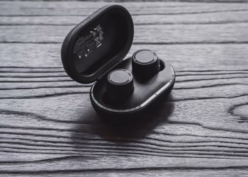 Close-up of true wireless earbuds in an open charging case on a textured wooden surface.