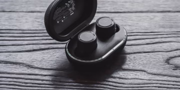 Close-up of true wireless earbuds in an open charging case on a textured wooden surface.
