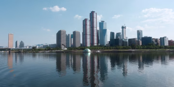 A stunning Seoul skyline reflecting in the river under a clear blue sky.