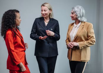 Three women in business attire having a conversation indoors, showcasing diversity and teamwork.