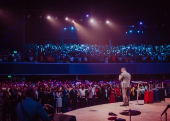A speaker in a gray suit captivates a large crowd on stage during a motivational event.