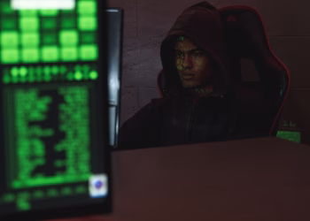 Hooded programmer intensely focused on computer screen, ensuring data protection and cyber security.
