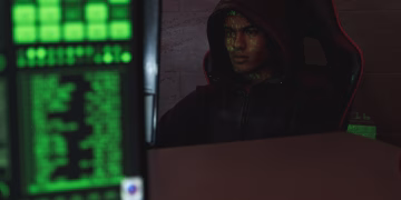Hooded programmer intensely focused on computer screen, ensuring data protection and cyber security.