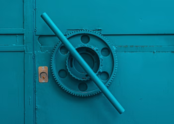 Close-up of a teal metal door with industrial gear mechanism, showcasing intricate machinery details.