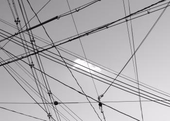 Low angle of black and white wires of high power against cloudy sky