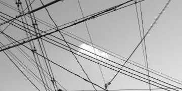 Low angle of black and white wires of high power against cloudy sky